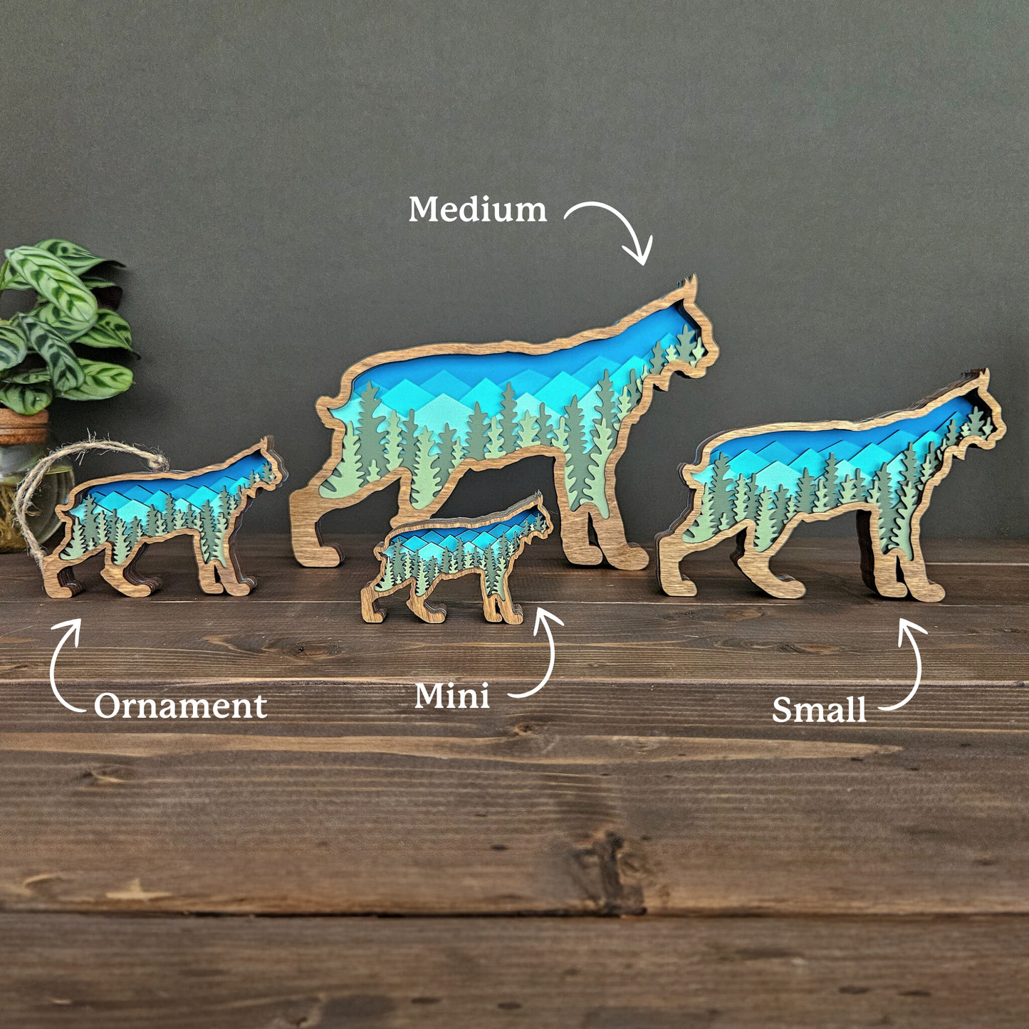 Set of four Bobcat or Lynx art pieces and ornament in different sizes on a wooden surface with a muted green background.