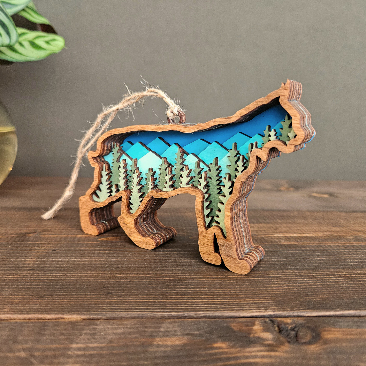 3D layered bobcat Christmas ornament side view at an angle with mountains and trees in laid within the silhouette