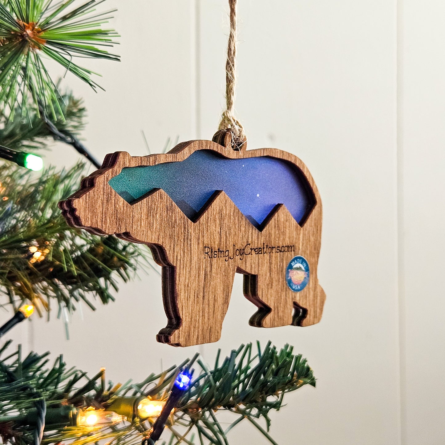 Wooden bear-shaped ornament with blue interior hanging on a Christmas tree.