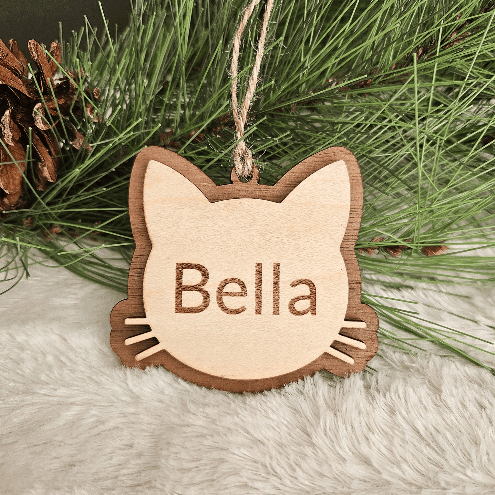 Wooden cat-shaped ornament with 'Bella' engraved, hanging on a Christmas tree.
