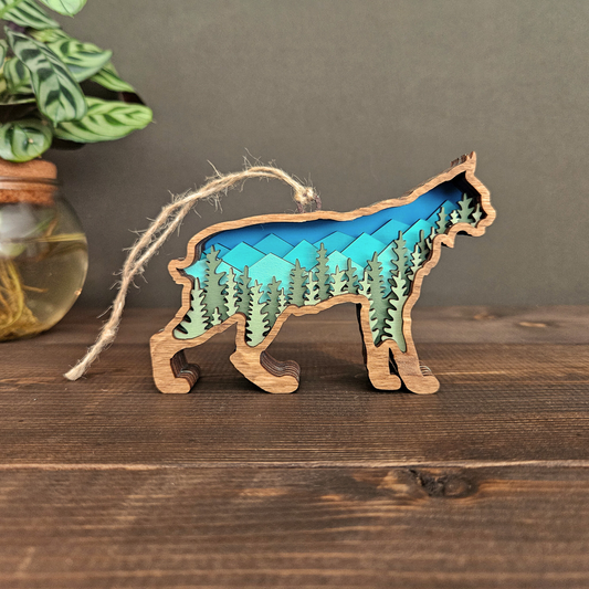 3D layered wood bobcat ornament with mountain and forest scene, handmade nature-inspired Christmas ornament standing upright on wood surface