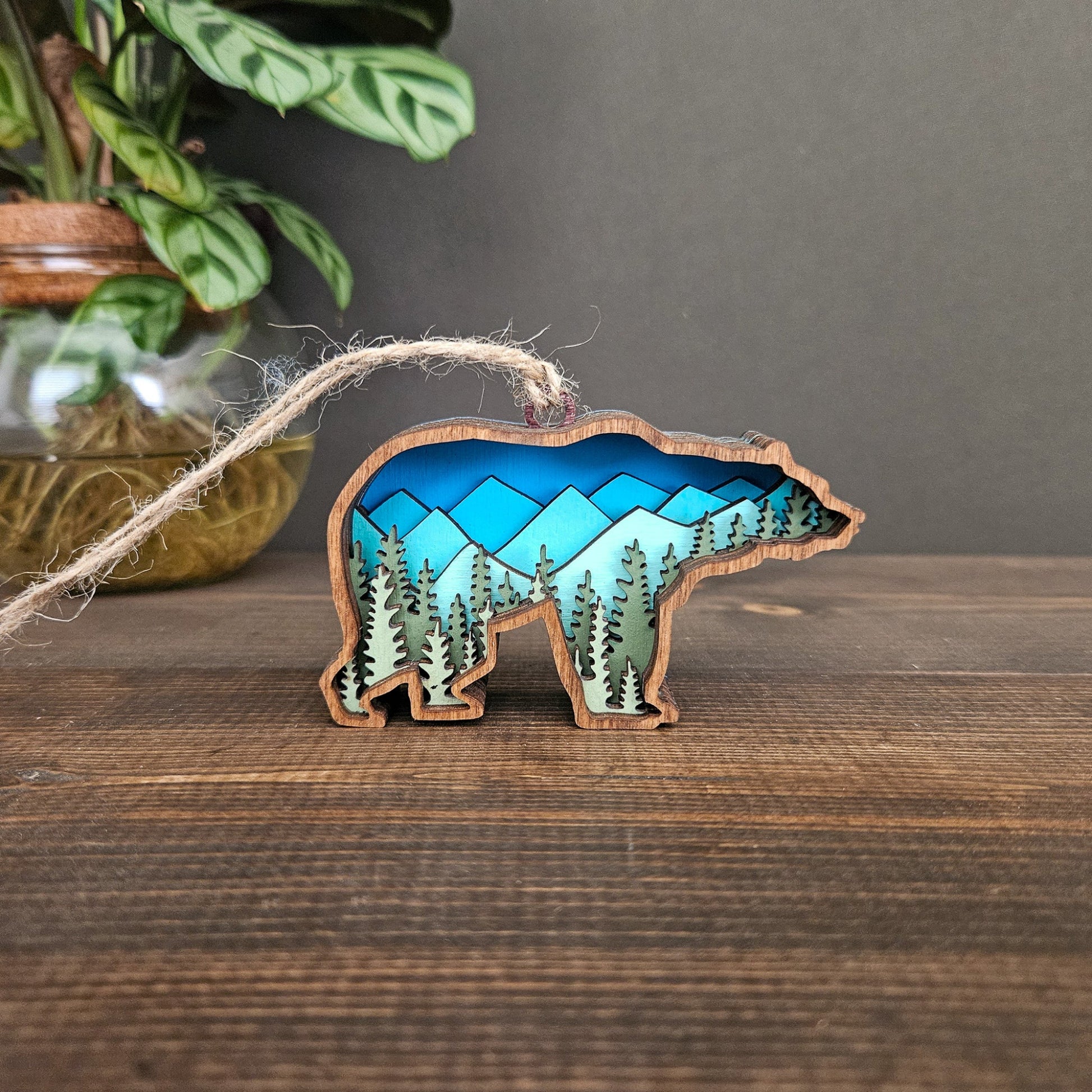 Decorative bear ornament with blue mountains and green tree design inside outline on a wooden surface