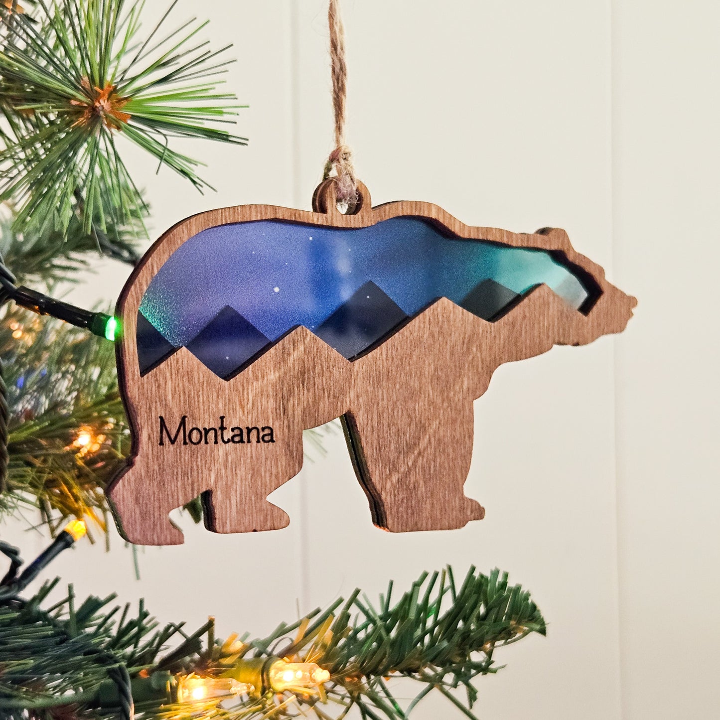 Wooden bear ornament with mountain design and 'Montana' text, hanging on a Christmas tree.