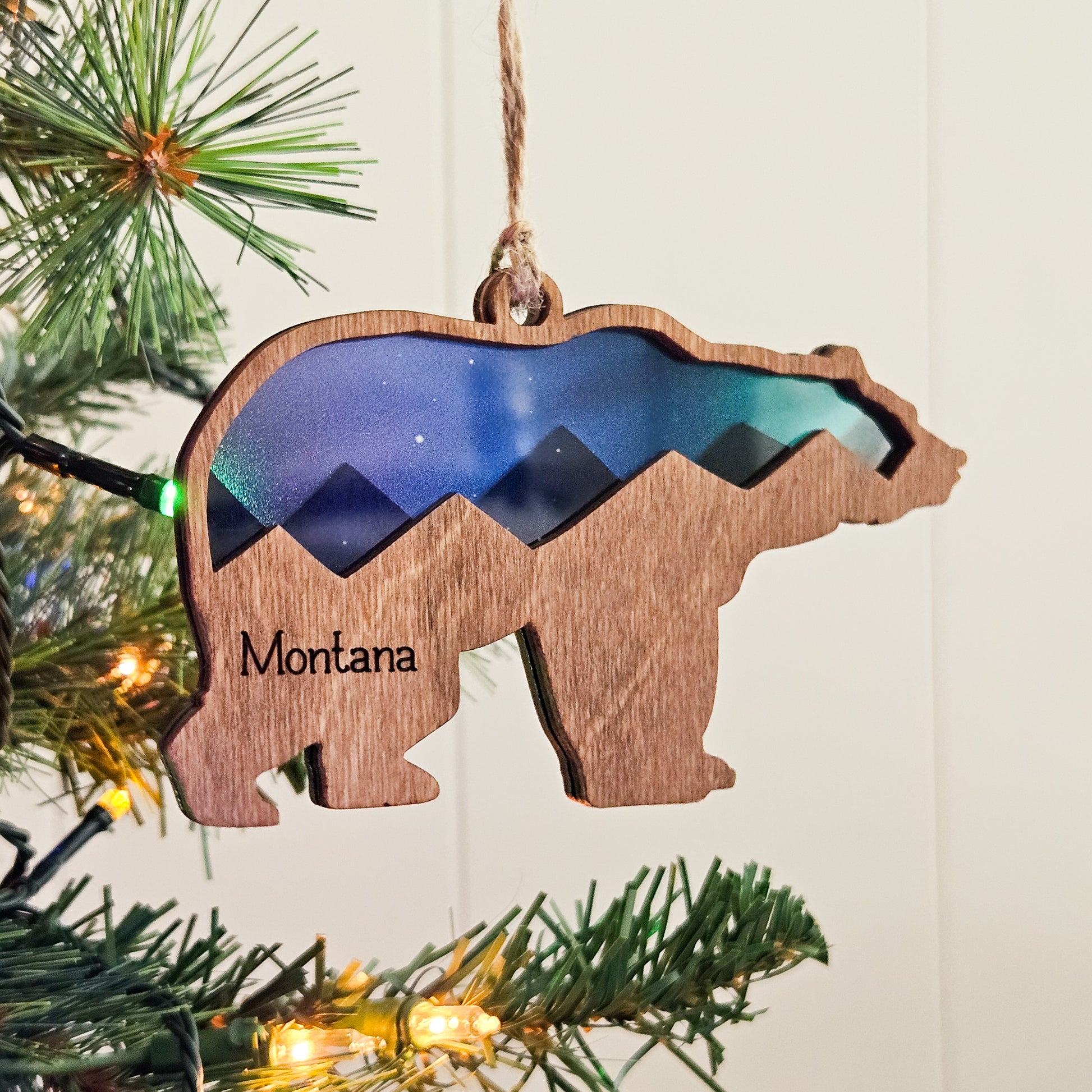 Wooden bear ornament with mountain design and 'Montana' text, hanging on a Christmas tree.