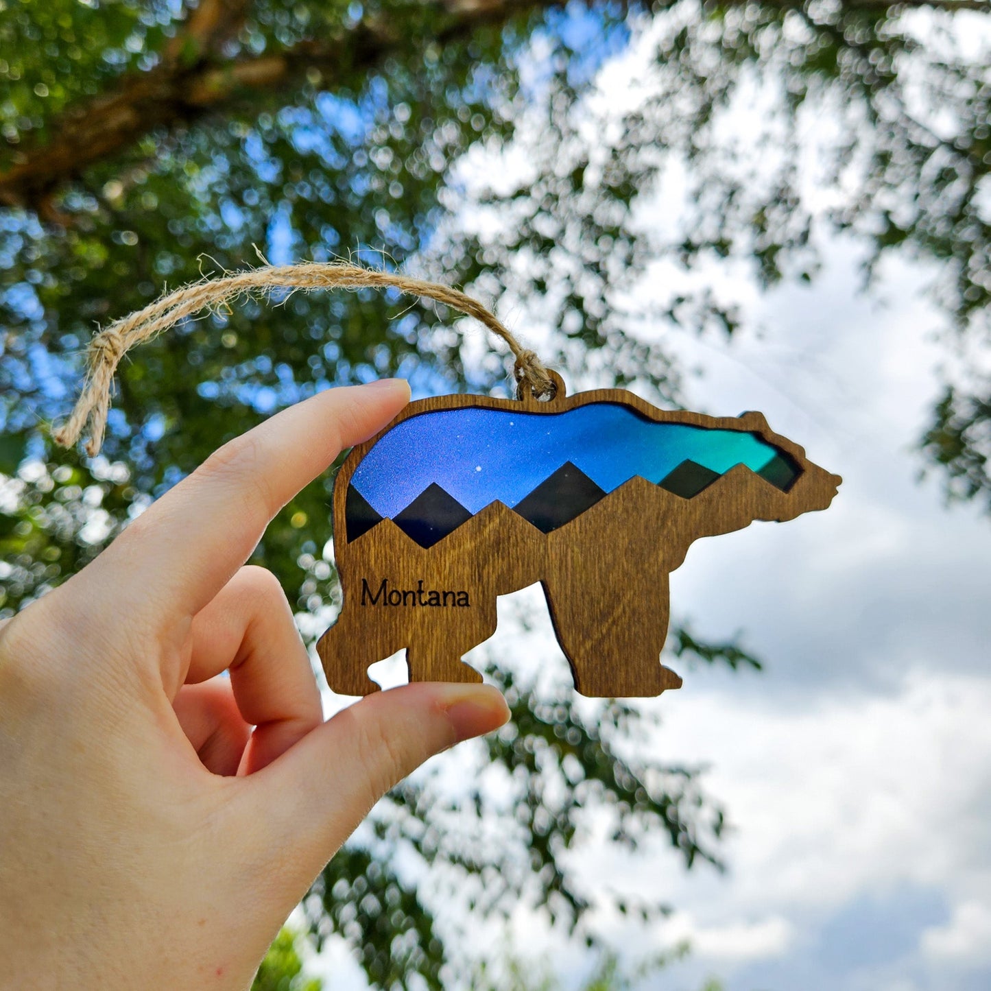 Wooden bear ornament with mountain design and 'Montana' text, held against a natural background.