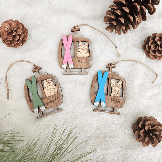 Wooden ornaments with skis and names on a white surface with pinecones and branches.