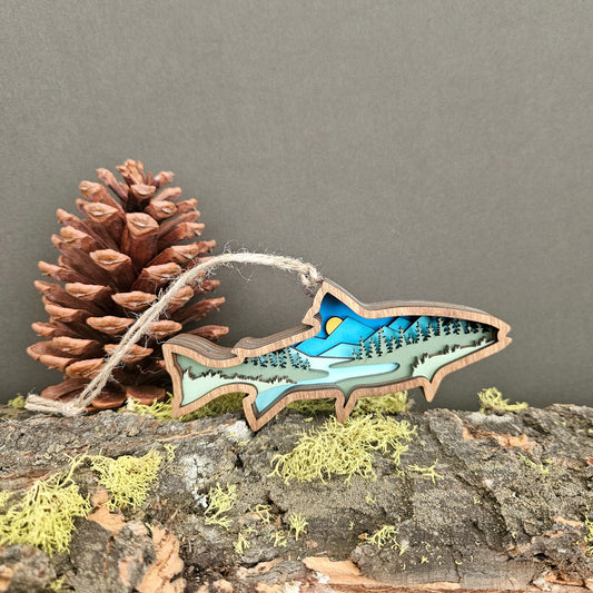 Wooden ornament shaped like a fish with a blue interior, placed on a rock with a pine cone and moss.