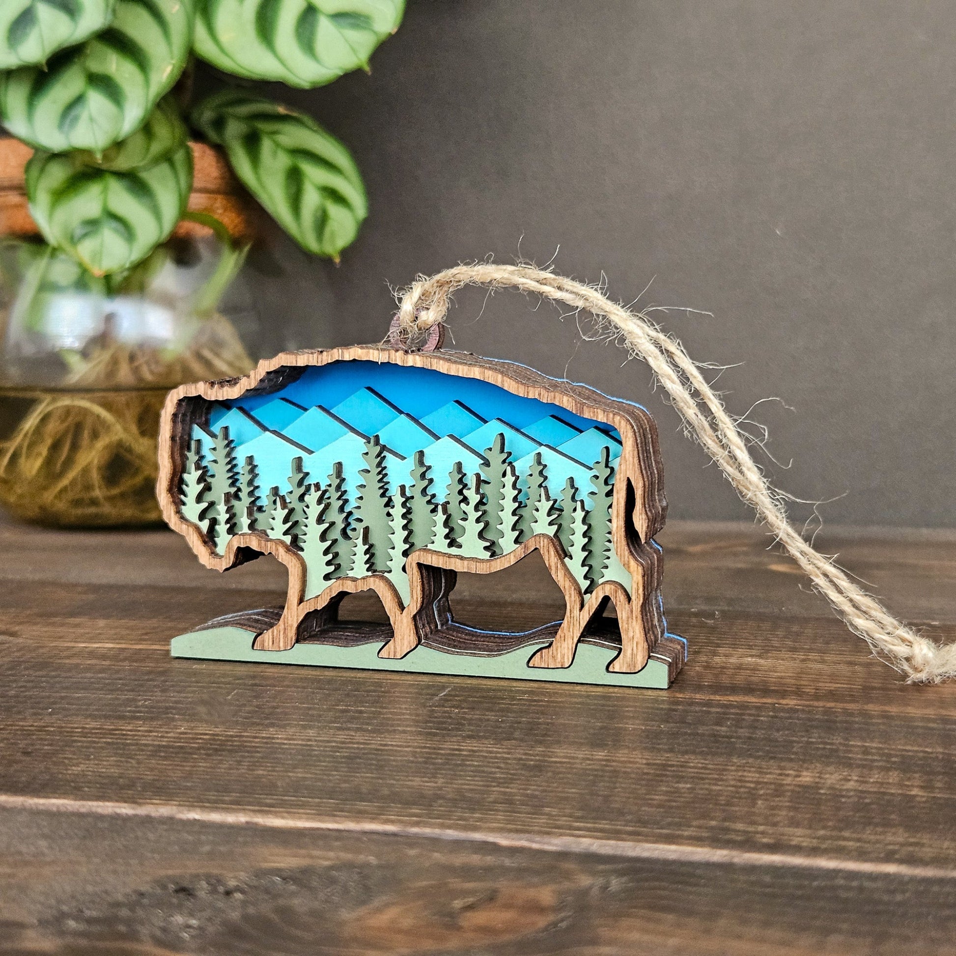 Wooden ornament shaped like a bear with a mountain and forest design, hanging on a string.