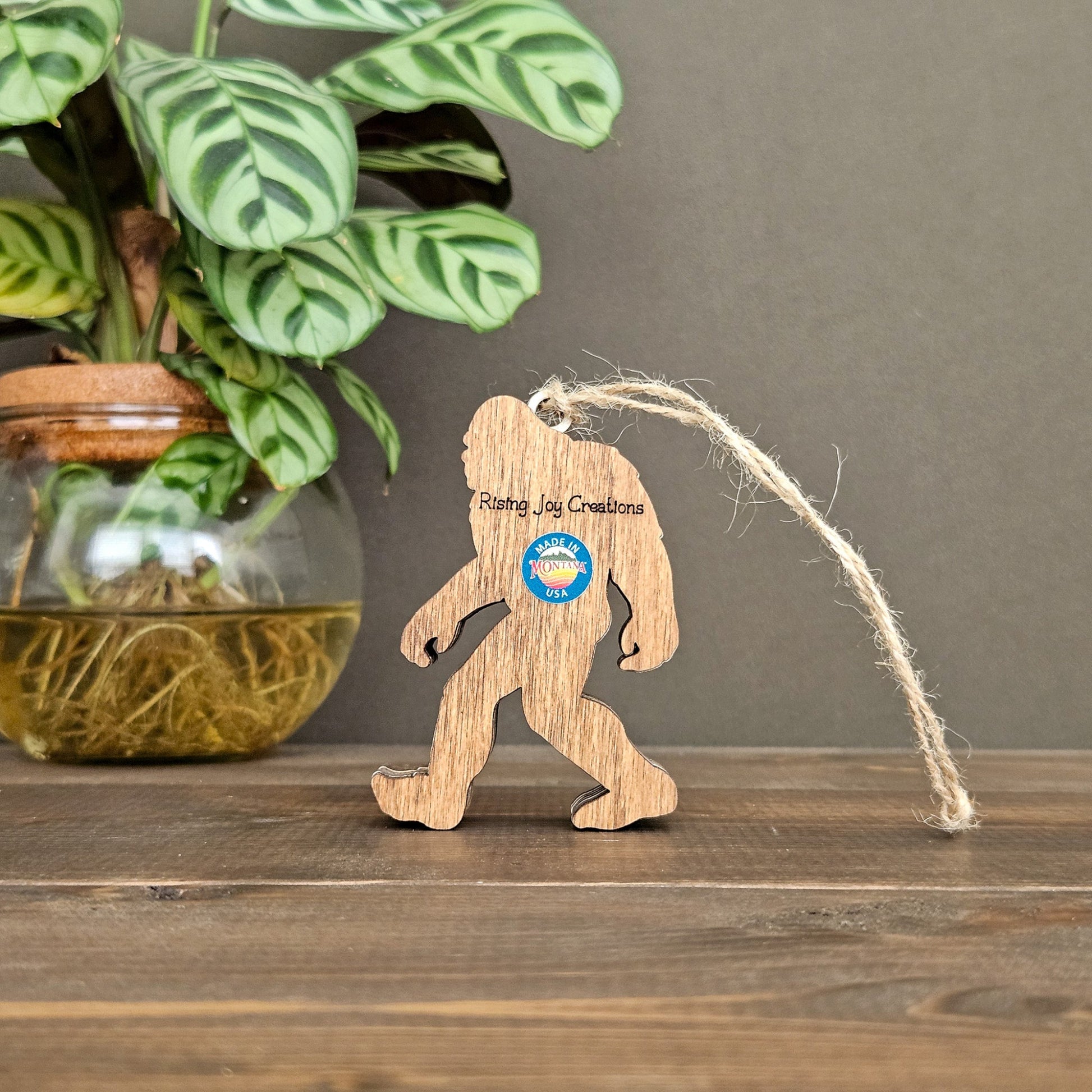 Wooden Bigfoot ornament with a brand logo on a wooden surface with a plant in the background