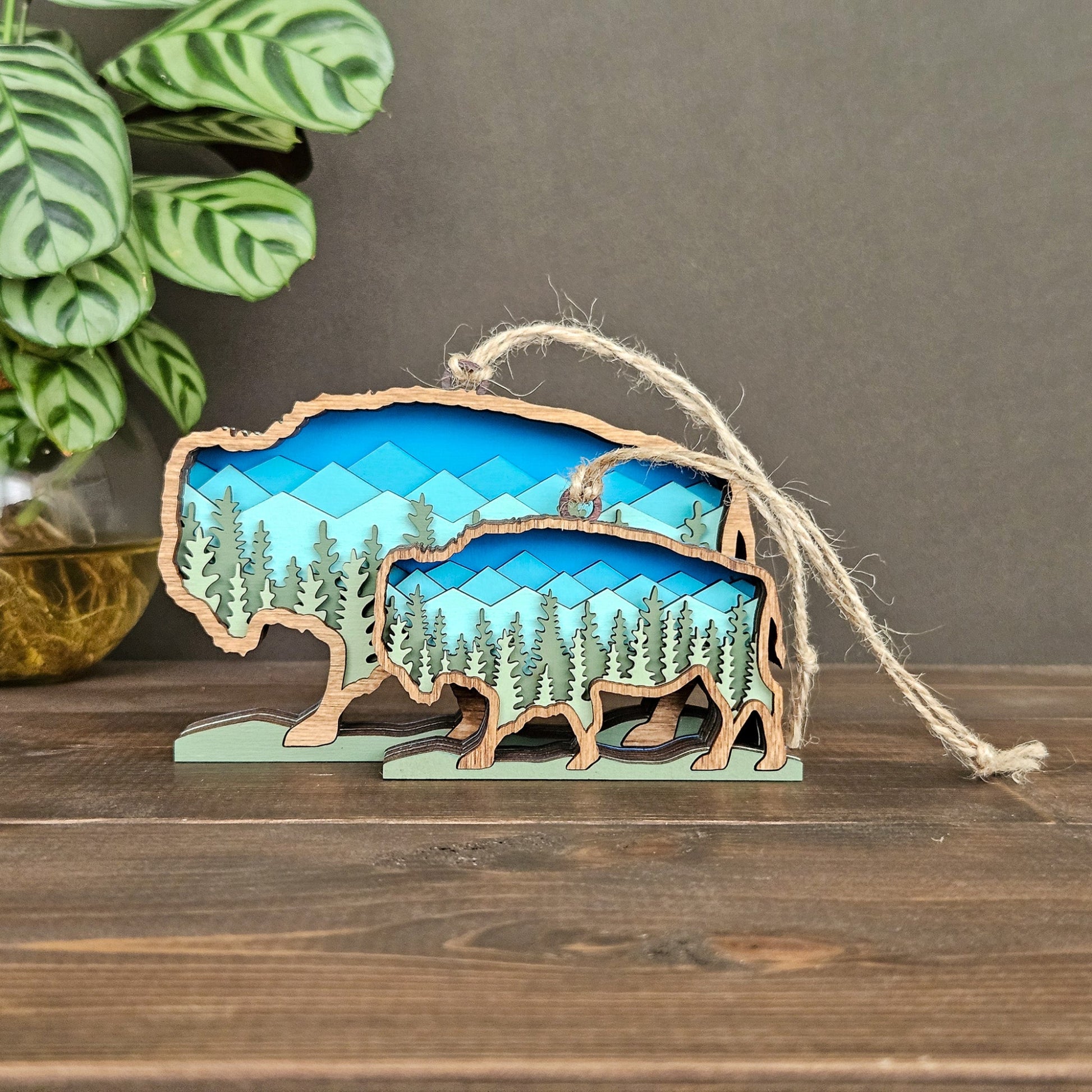 Wooden ornament shaped like a bear with a mountain and forest design, hanging on a string.