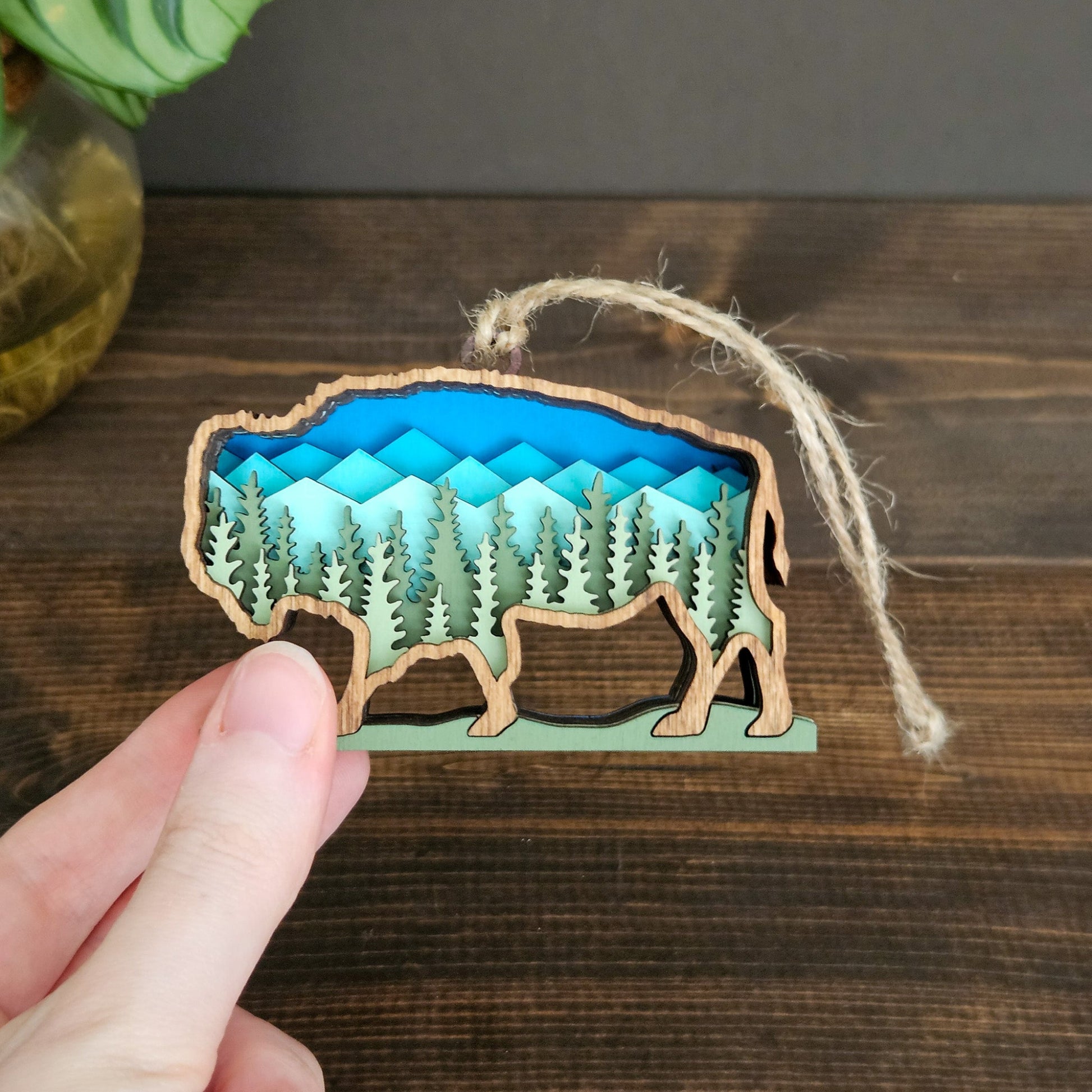 Wooden ornament shaped like a bear with a forest design on a wooden surface.