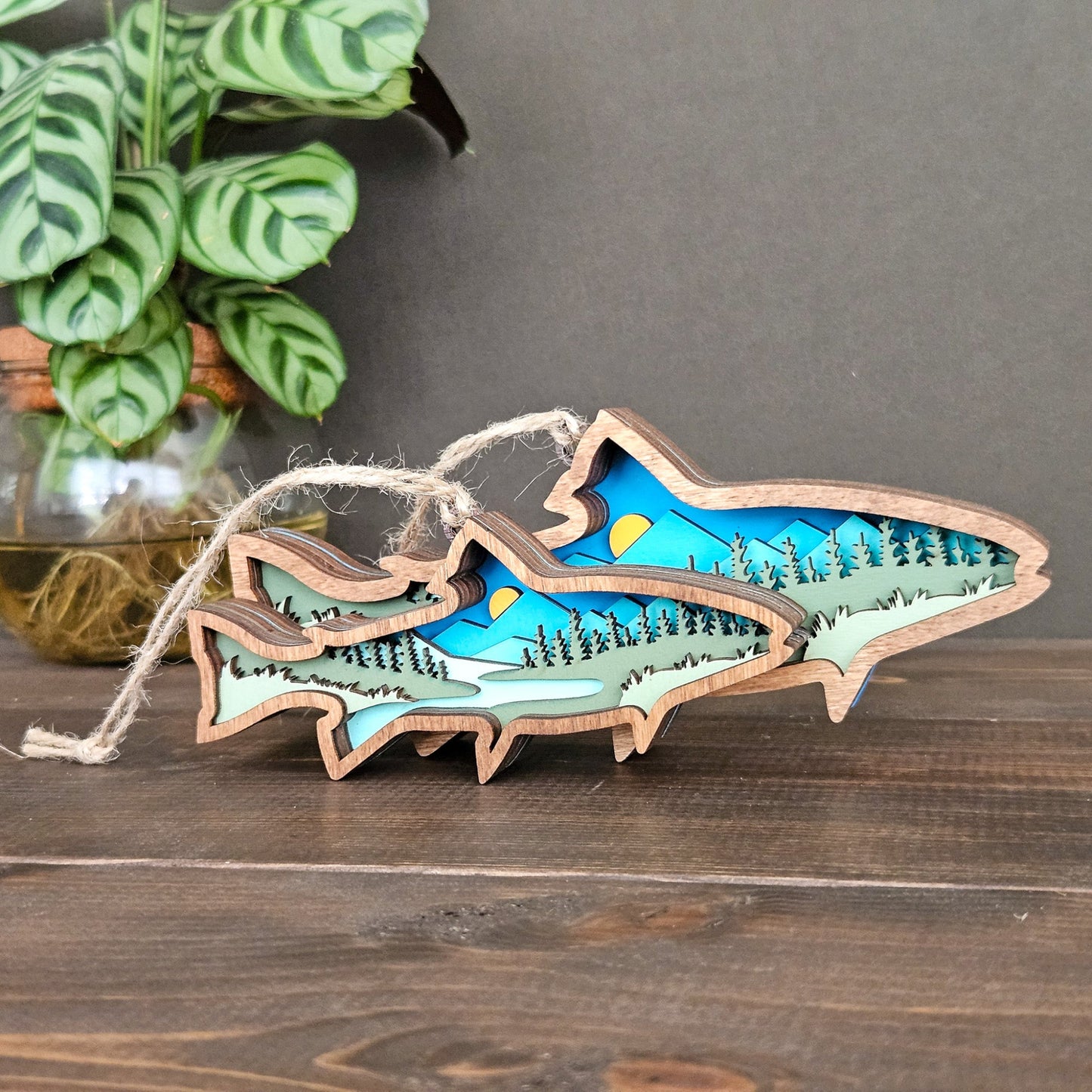 Wooden ornament with mountain and lake design on a wooden surface with a plant in the background