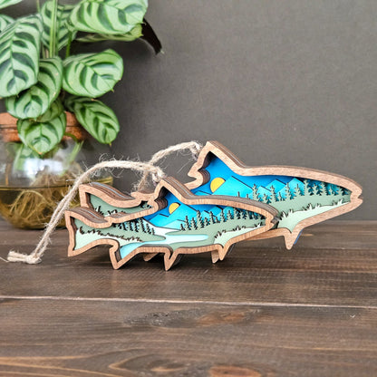 Wooden ornament with mountain and lake design on a wooden surface with a plant in the background