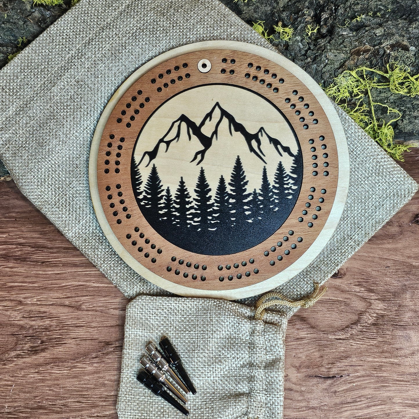 Wooden cribbage board with mountain and tree design on a wooden surface with pegs.