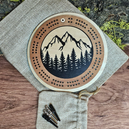 Wooden cribbage board with mountain and tree design on a wooden surface with pegs.