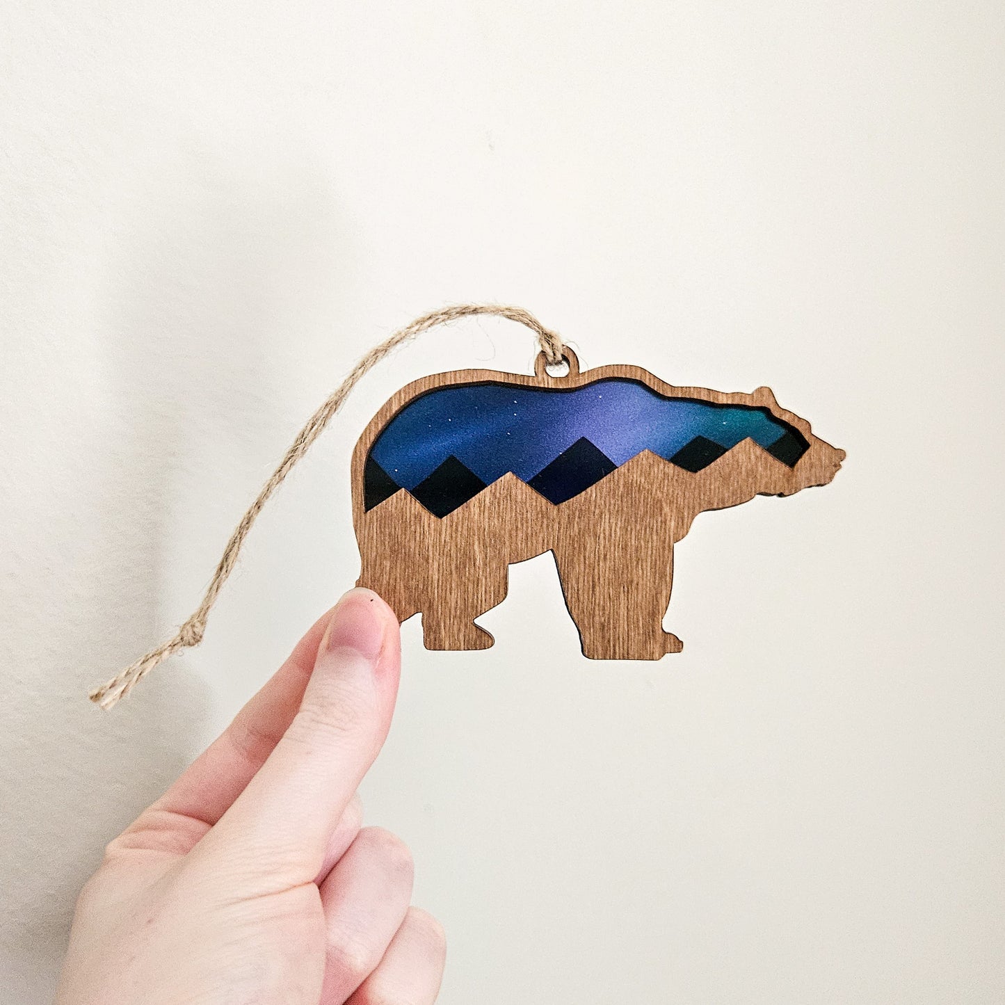 Wooden bear ornament with mountain design held by a hand against a plain background
