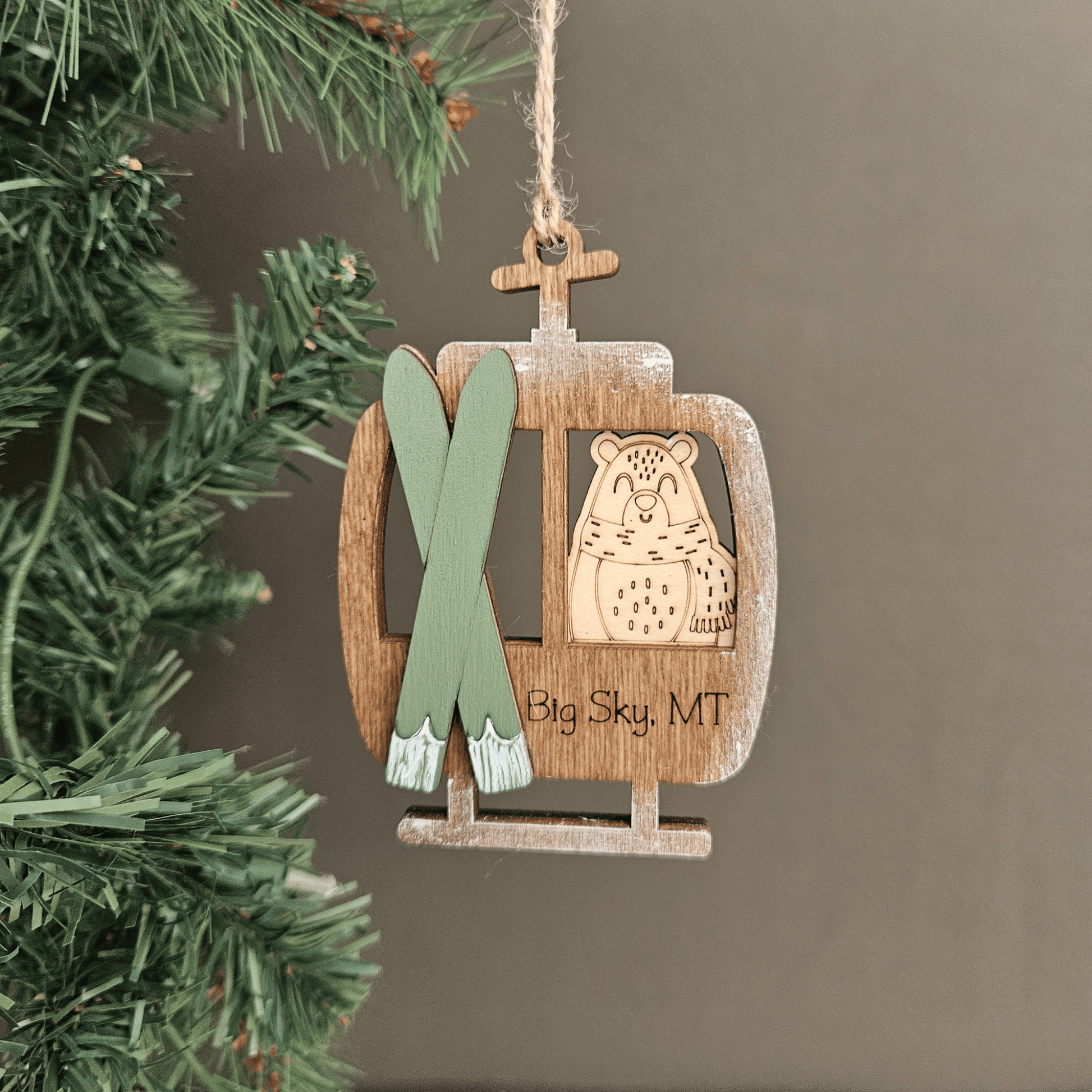 Wooden ornament shaped like a ski lift with skis and a bear design, hanging on a Christmas tree.