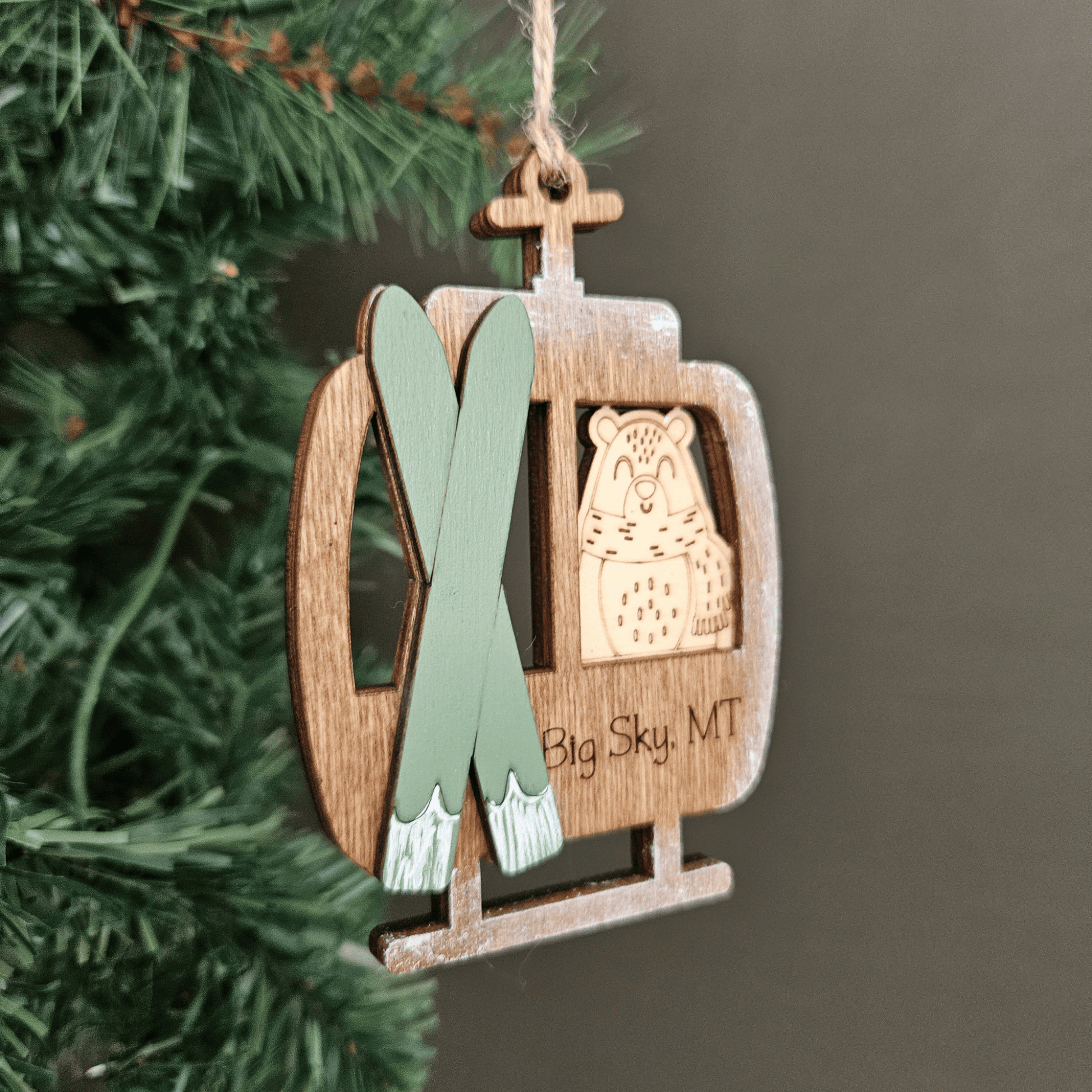 Wooden ornament shaped like a ski lift with skis and a bear emblem, hanging on a tree.