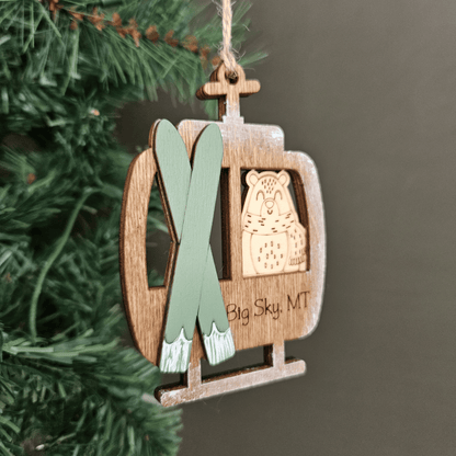 Wooden ornament shaped like a ski lift with skis and a bear emblem, hanging on a tree.