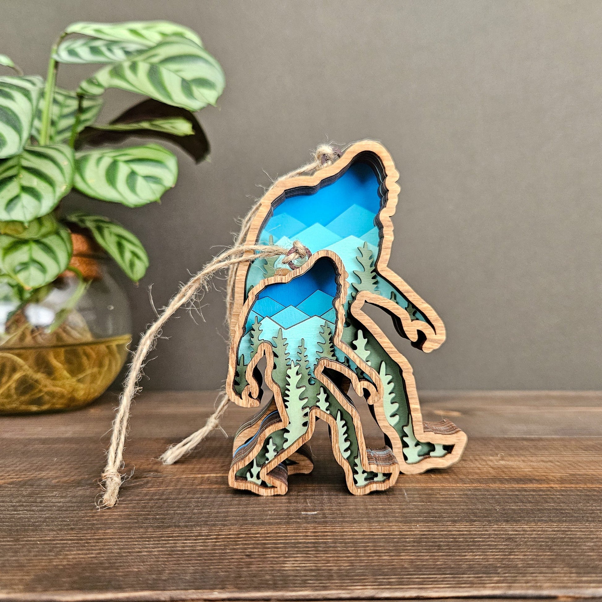 Wooden sasquatch figure with blue interior on a wooden surface, plant in the background