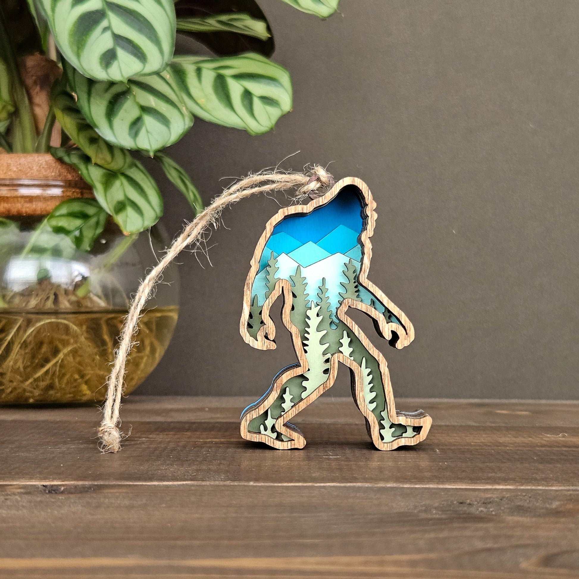 Sasquatch shaped ornament with a blue and green pattern, hanging on a string against a neutral background.