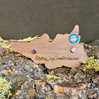 A wooden cutout sign shaped like Tennessee, engraved with 'RisingJoyCreations.com' on the back and a blue circular 'Made in USA' sticker, displayed on textured bark with moss.