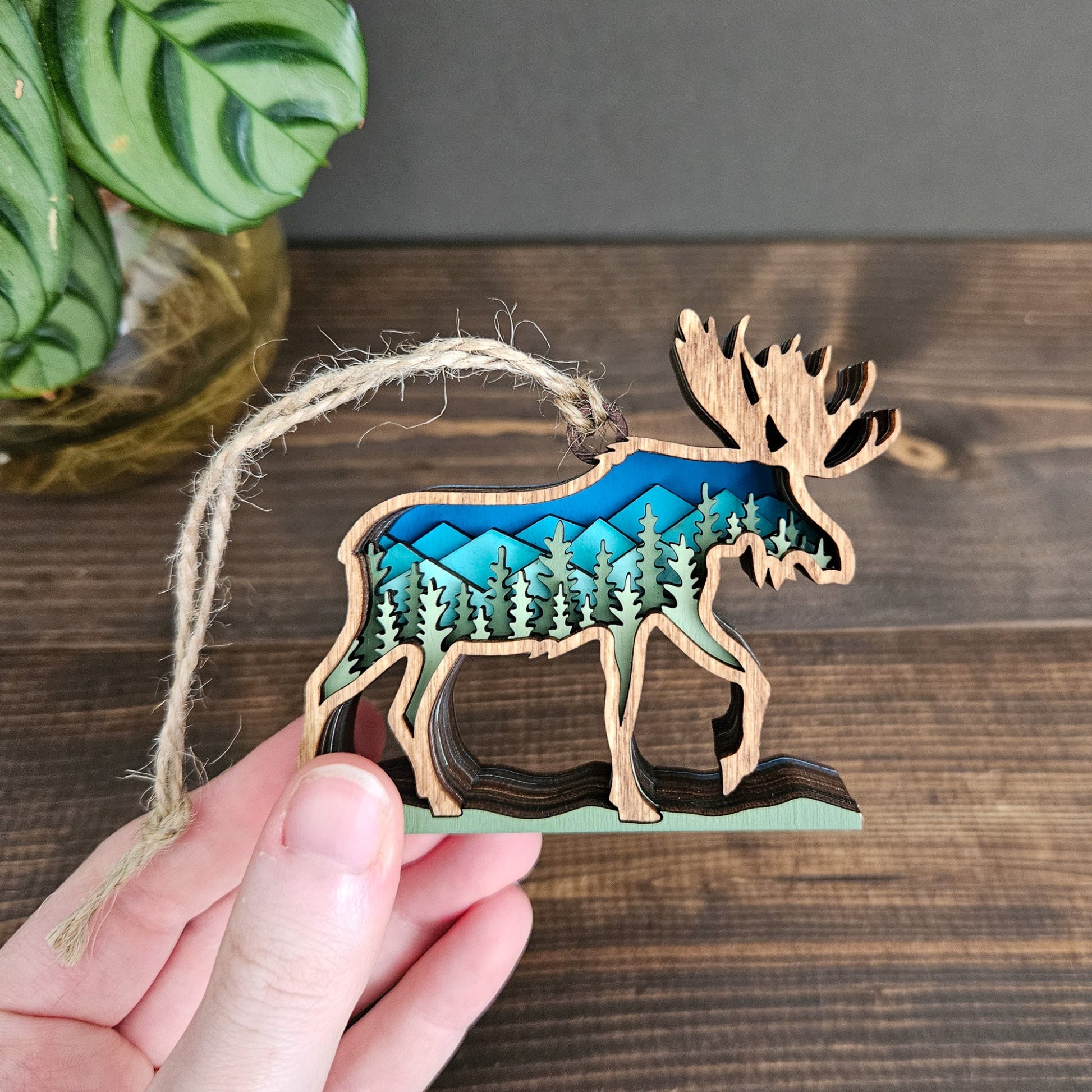 Wooden ornament shaped like a moose with a forest design on a wooden surface.
