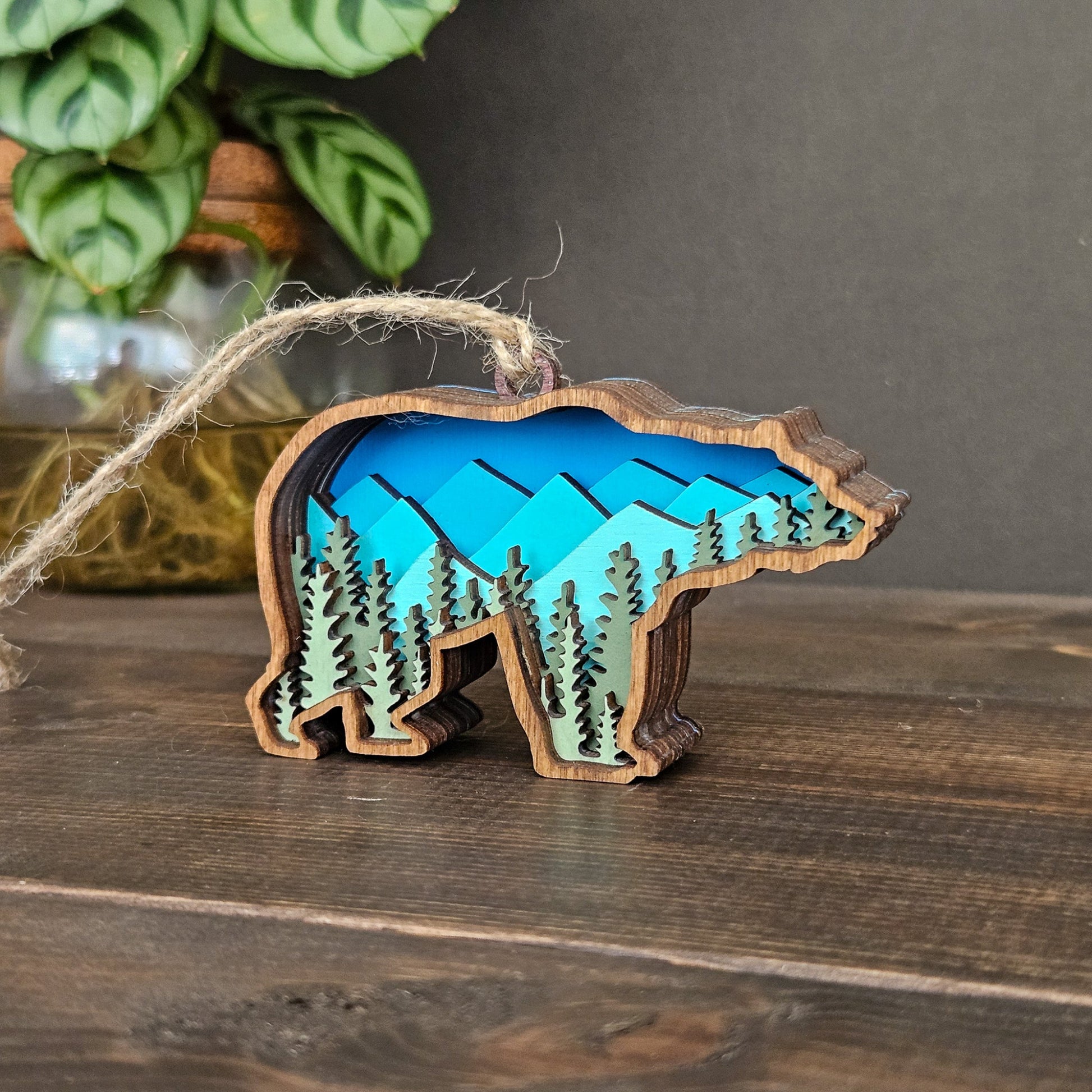Wooden bear ornament with mountain and forest design on a wooden surface