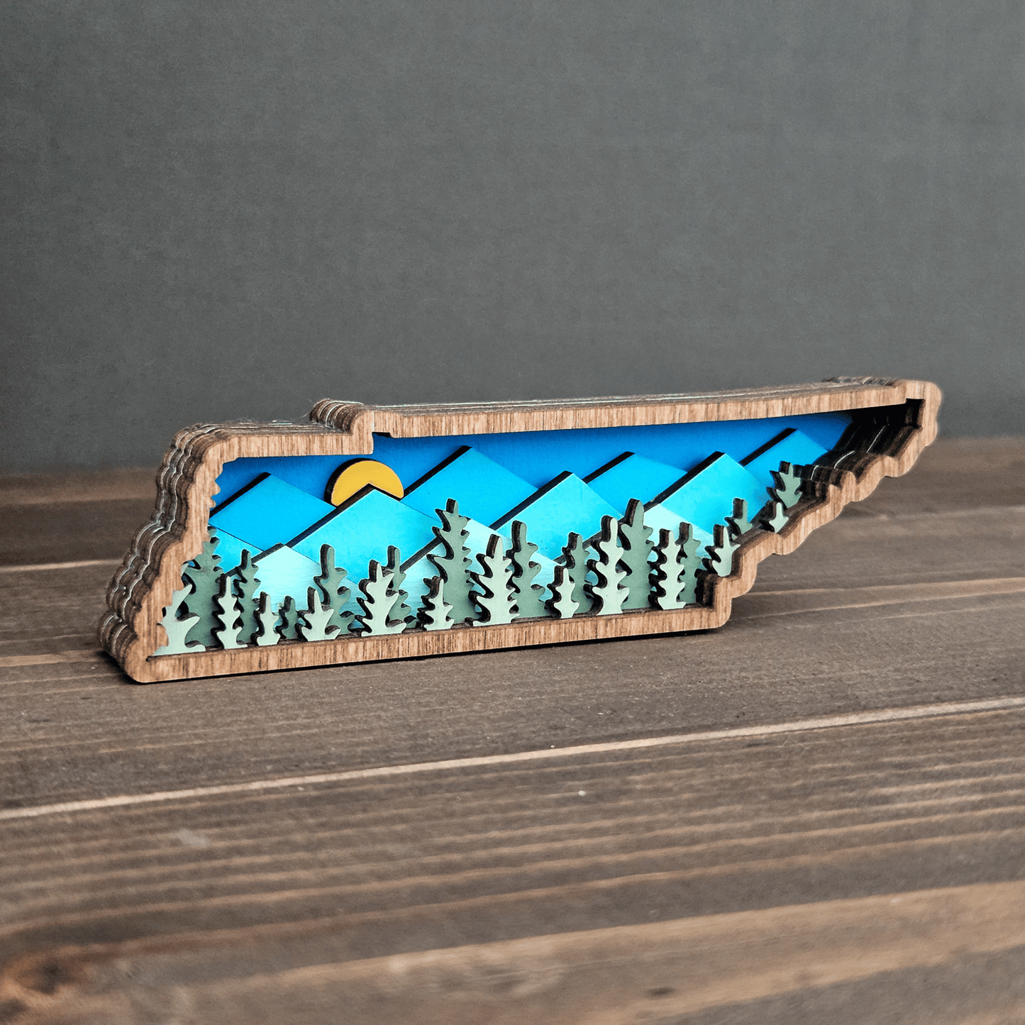 Angled front view of mini Tennessee magnet with sunrise over layered blue mountains and forest cutouts — handmade wood decor.