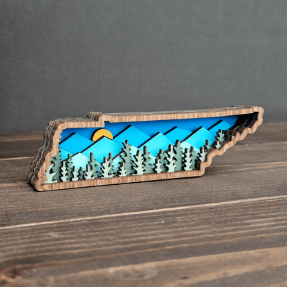 Angled front view of mini Tennessee magnet with sunrise over layered blue mountains and forest cutouts — handmade wood decor.