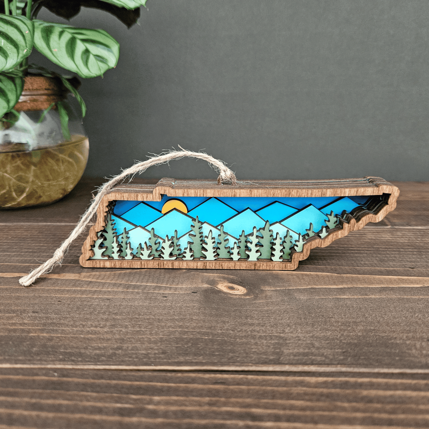 Handcrafted Tennessee ornament with layered blue mountains and trees — rustic wooden state decoration with jute twine hanger.