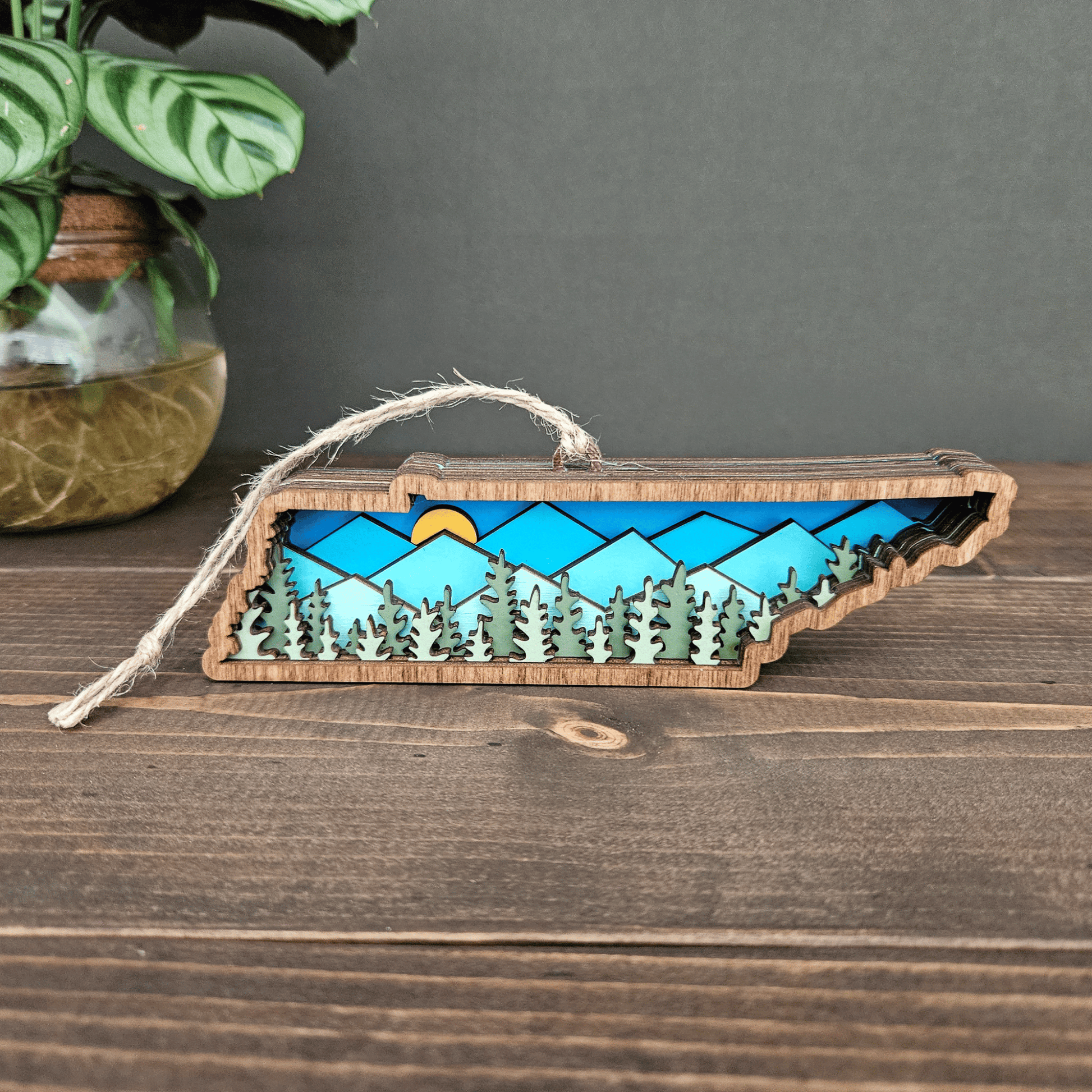 Handcrafted Tennessee ornament with layered blue mountains and trees — rustic wooden state decoration with jute twine hanger.