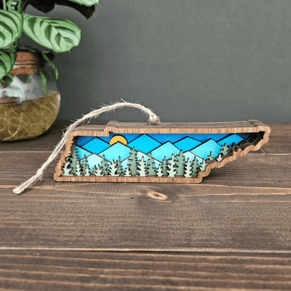 Handcrafted Tennessee ornament with layered blue mountains and trees — rustic wooden state decoration with jute twine hanger.