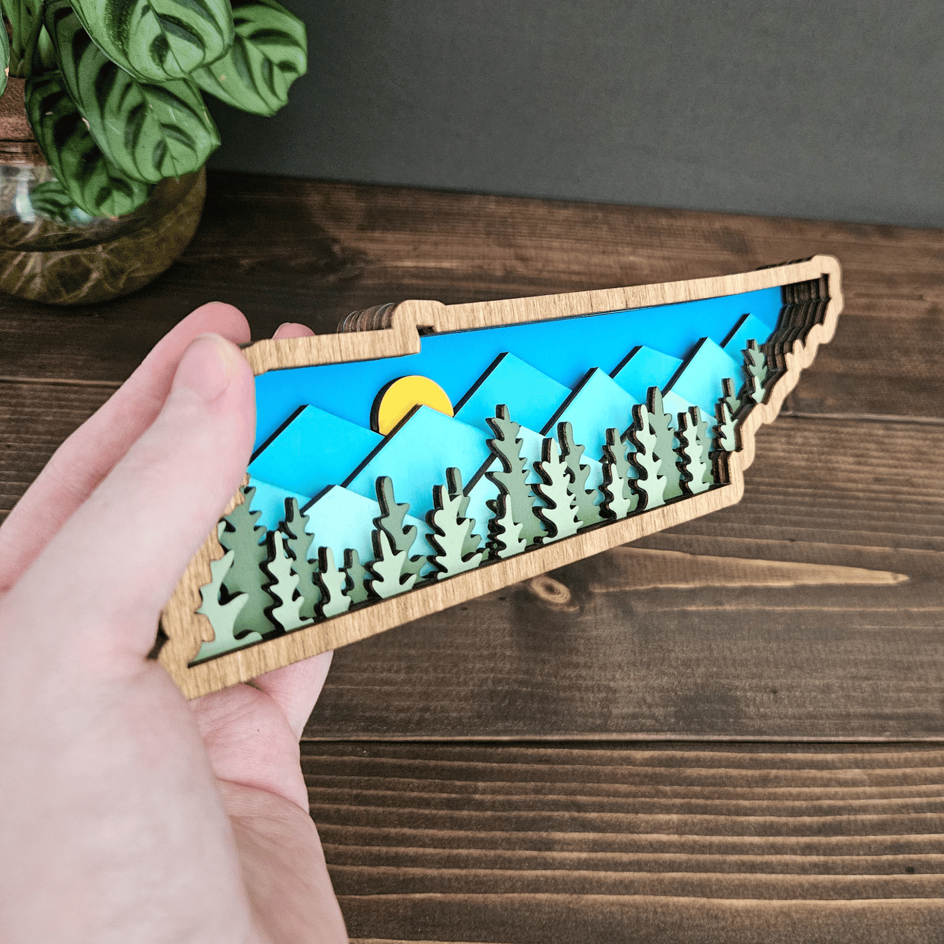 Close-up of Tennessee layered wood art showing mountain details, forest cutouts, and bright sky background.