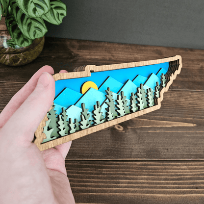 Close-up of Tennessee layered wood art showing mountain details, forest cutouts, and bright sky background.