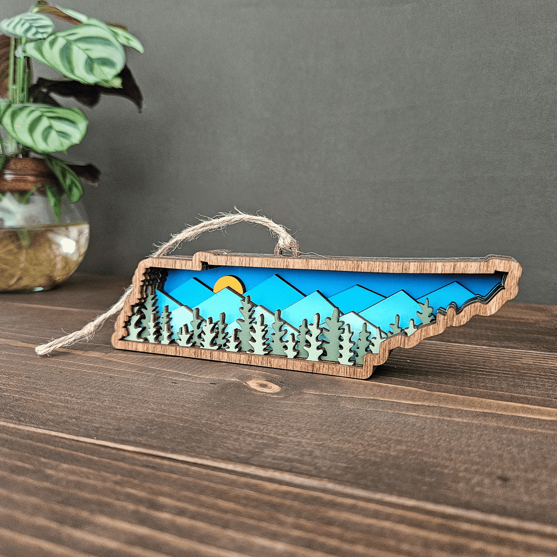 Front view of layered Tennessee mountain ornament showing forest and sunrise design — handcrafted wood state decor by Rising Joy Creations.