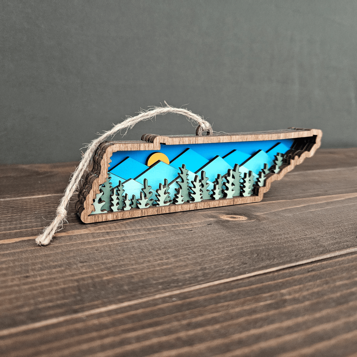 Angled side view of Tennessee mountain ornament showing 3D layered forest and sun detail — handmade wood state keepsake.