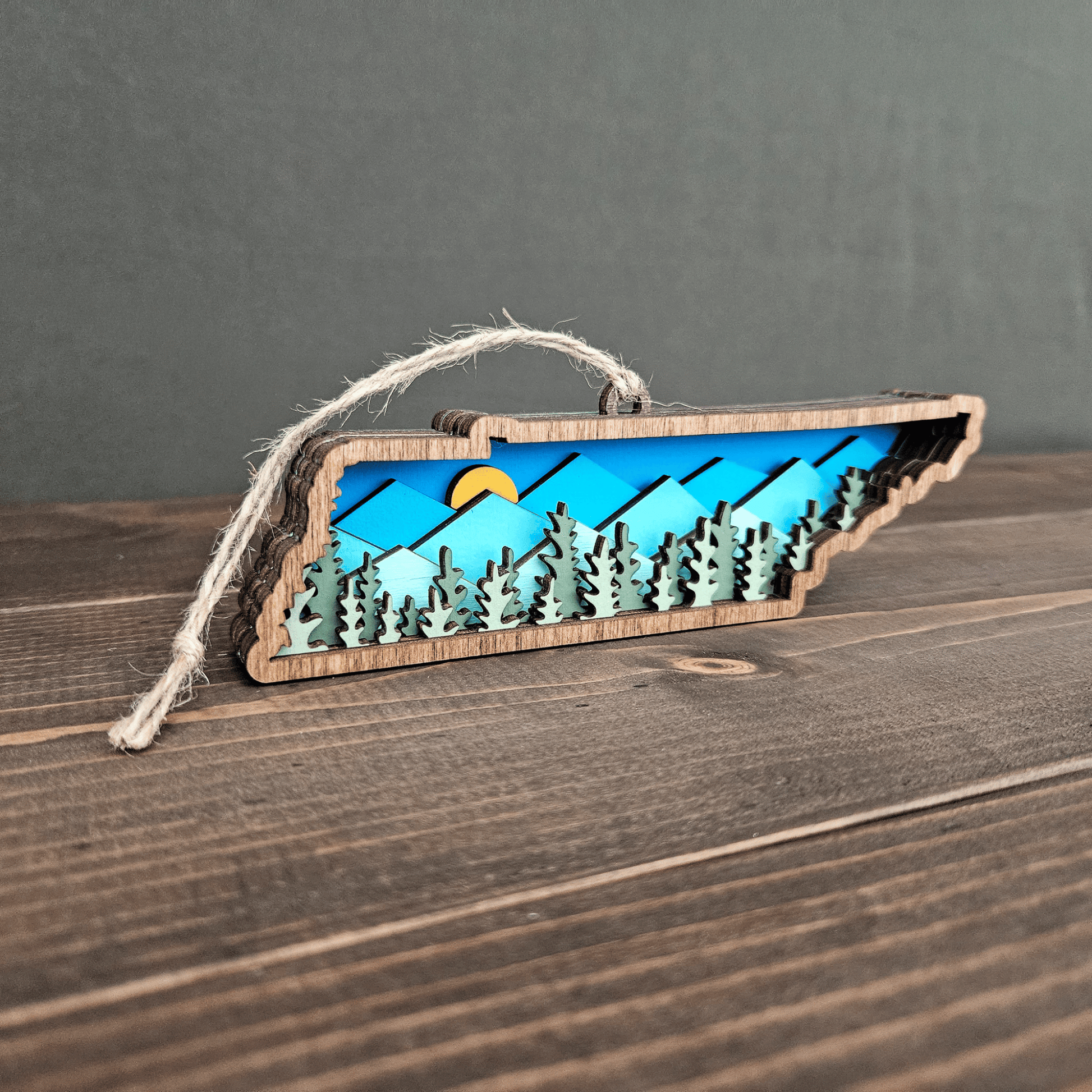 Angled side view of Tennessee mountain ornament showing 3D layered forest and sun detail — handmade wood state keepsake.