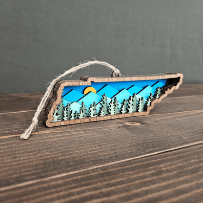 Angled side view of Tennessee mountain ornament showing 3D layered forest and sun detail — handmade wood state keepsake.
