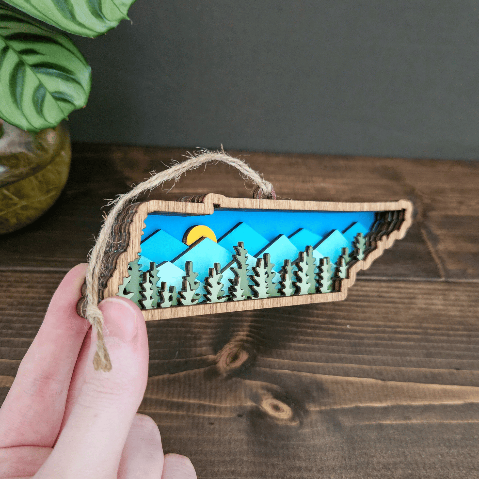 Close-up of Tennessee mountain ornament showing layered forest detail and blue mountain backdrop — handmade wooden decor.