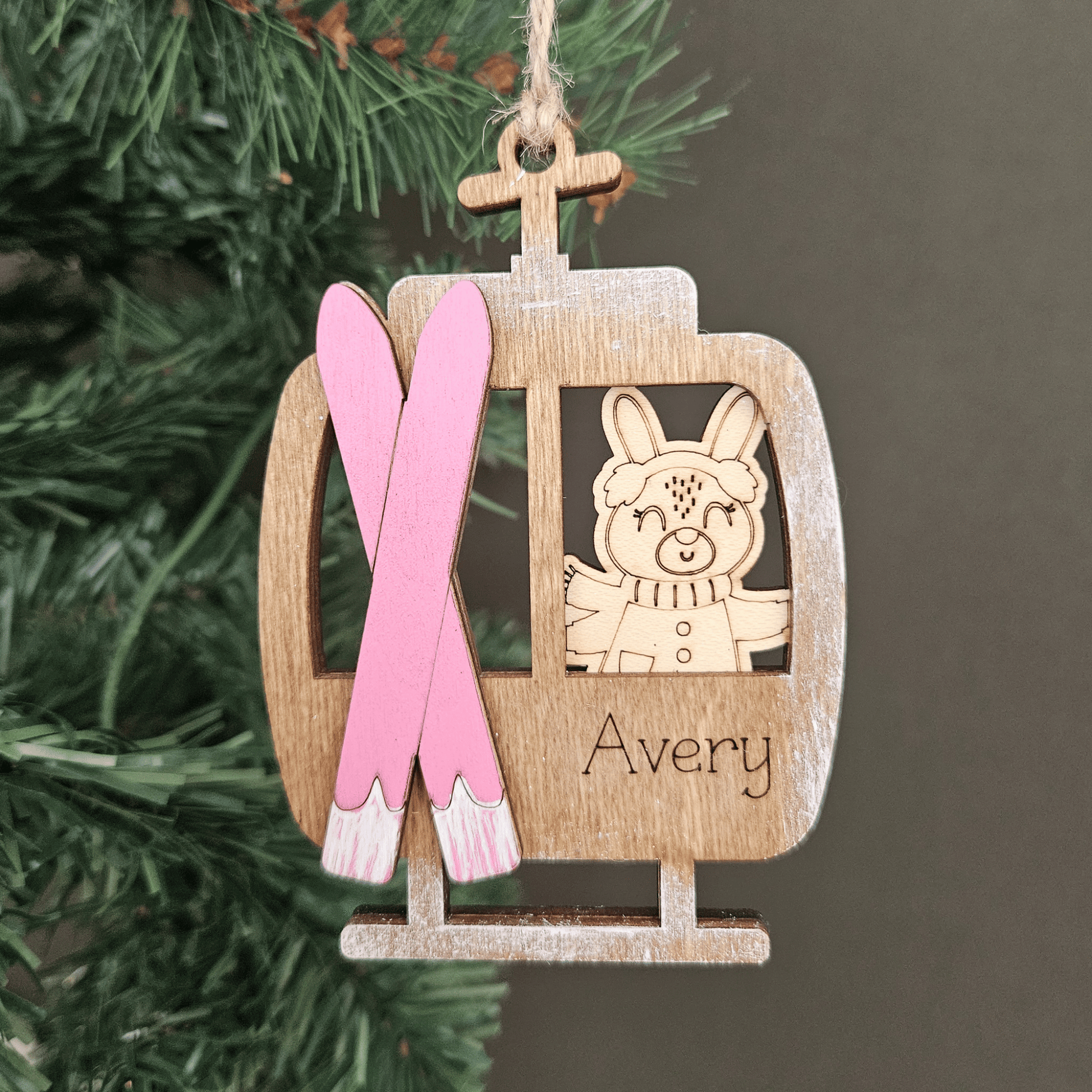 Wooden ornament with pink skis and a cartoon bunny, hanging on a Christmas tree.