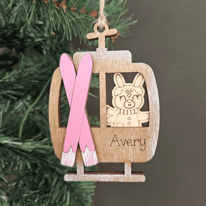 Wooden ornament with pink skis and a cartoon bunny, hanging on a Christmas tree.