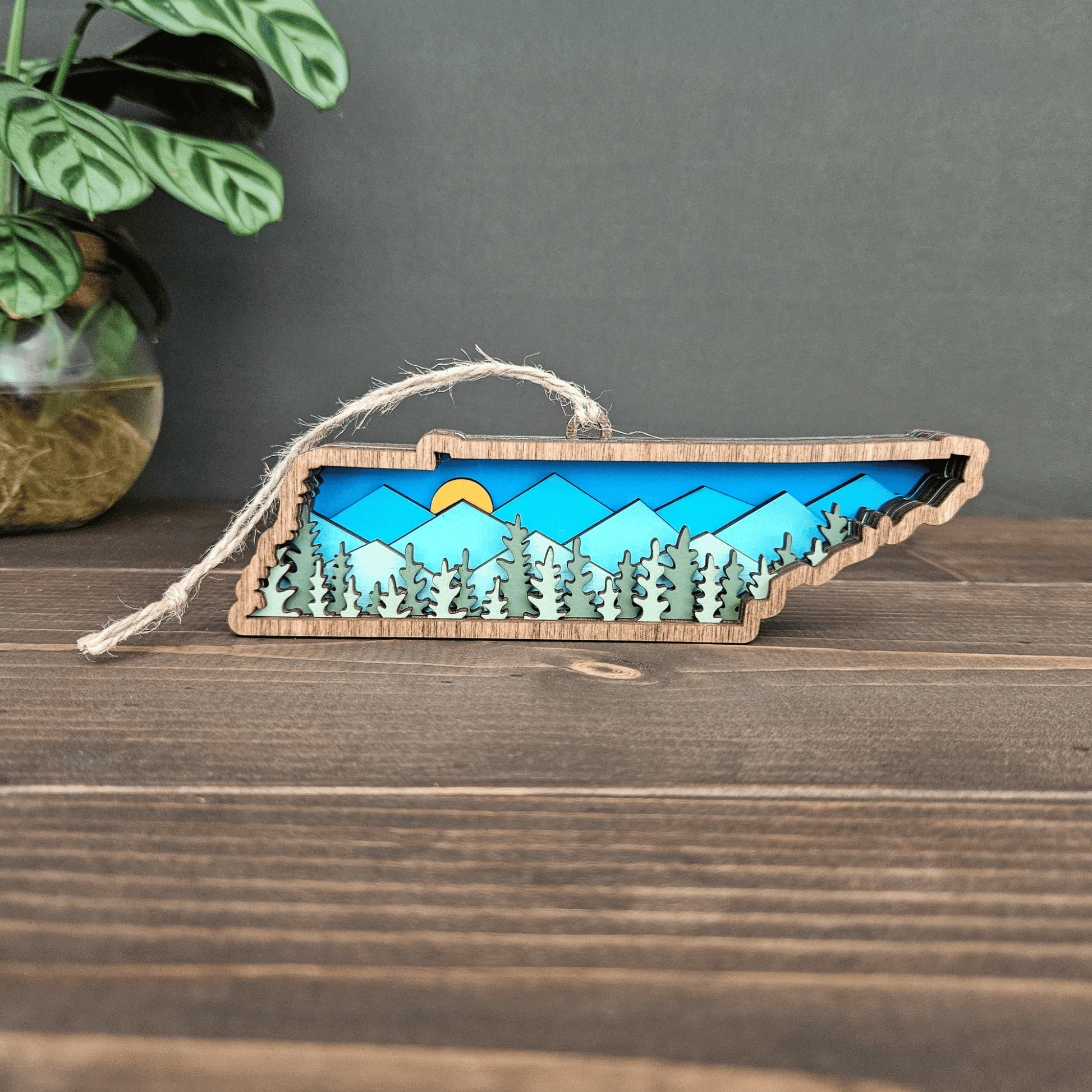 Layered Tennessee mountain ornament displayed on wood surface with jute twine — handcrafted rustic state decoration.