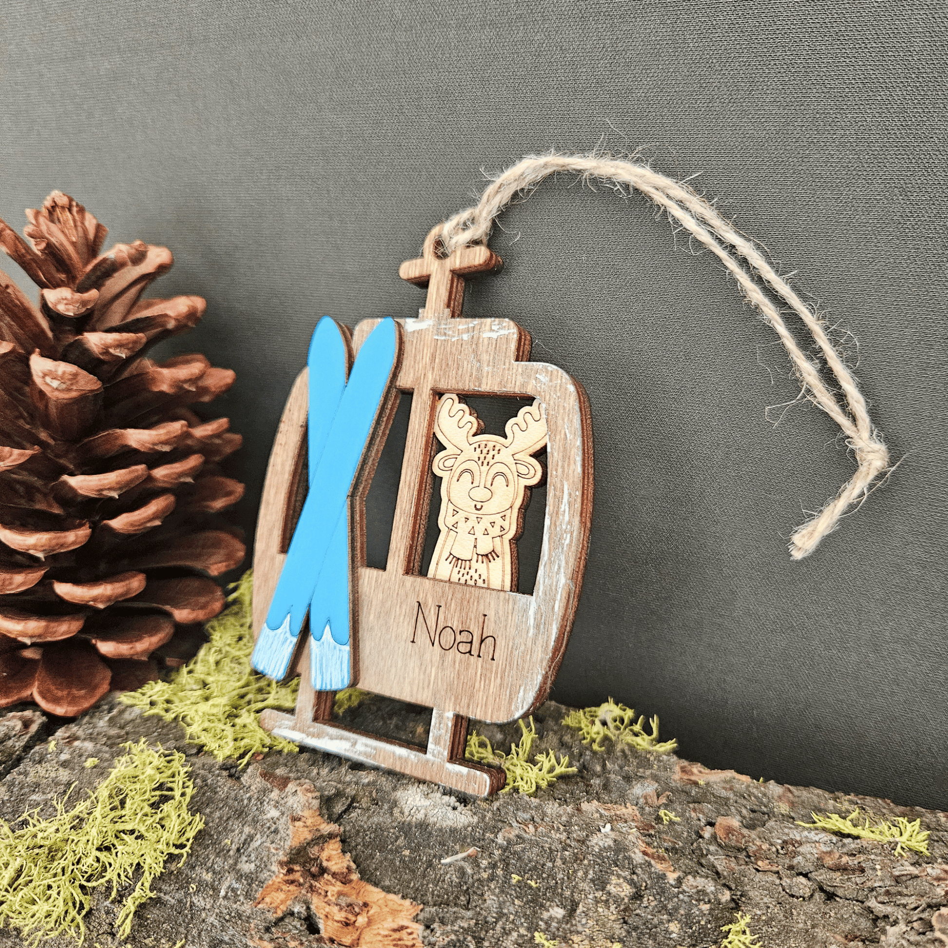 Wooden ornament with a reindeer design, blue skis, and the name 'Noah' on a dark background.